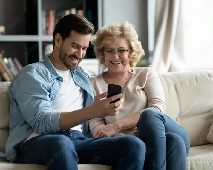 Son sitting with older mother at home looking at phone
